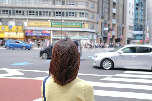 横断歩道で立ち止まっている女性の後ろ姿の画像