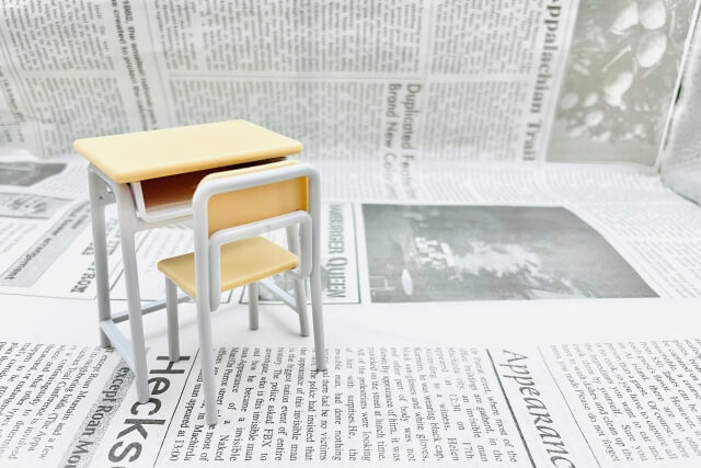 英字新聞と学校の机といすの画像